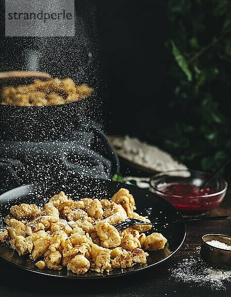 Kaiserschmarrn auf einem schwarzen Teller  wird mit Zucker bestreut  dunkler Hintergrund