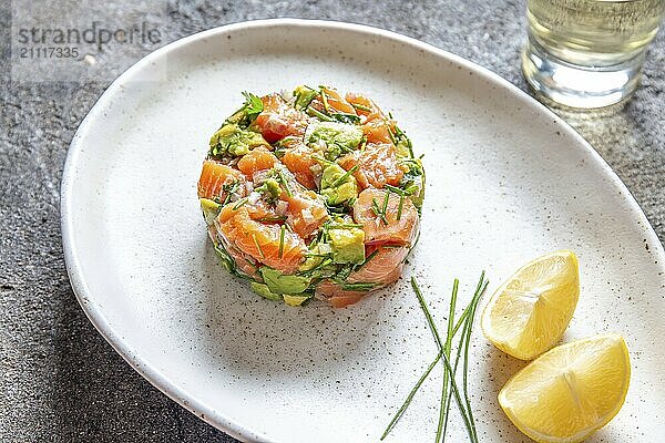 PERUVIANISCHES ESSEN. Lachs Ceviche mit Avocado  Frühlingszwiebeln und Zitrone auf weißem Teller  serviert mit Weißwein