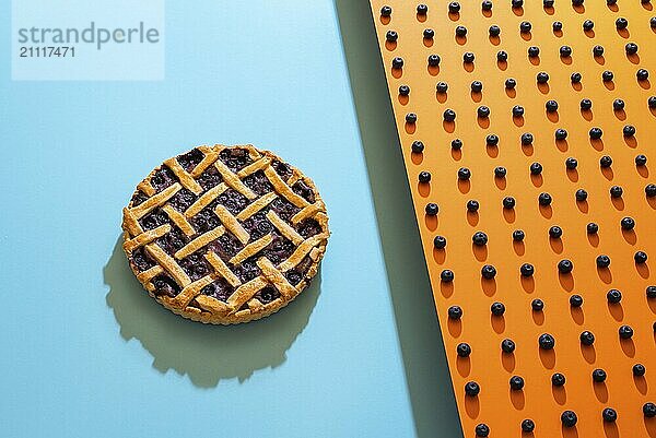 Klassische Heidelbeerkuchen mit Gitter Kruste auf blauem Hintergrund und Heidelbeeren Muster auf orangem Hintergrund. Ein Beerenkuchen und die Hauptzutat