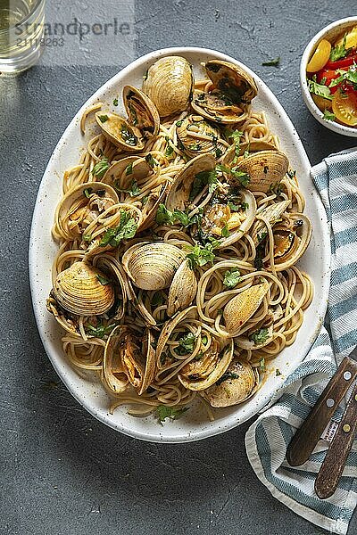 Nudeln mit Meeresfrüchten. ITALIENISCHE SPAGHETTI ALLE VONGOLE. Spaghetti mit Venusmuscheln auf weißem Teller mit Weißwein  grauer Hintergrund. Ansicht von oben