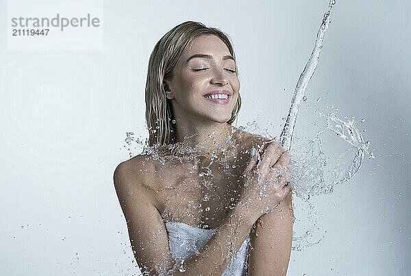 Junges glückliches Mädchen genießt den Wasserstrahl und die Spritzer  die von oben auf ihre Schulter fallen Studioaufnahme