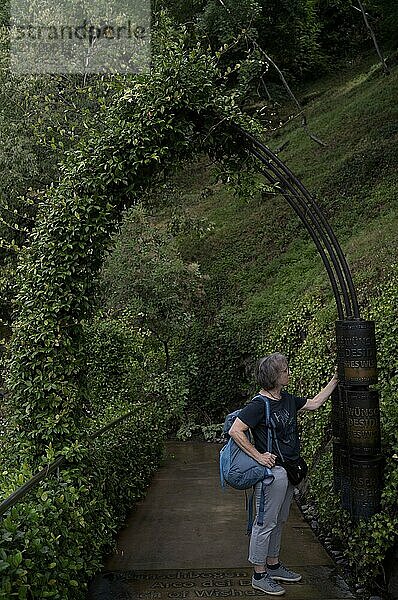 Ältere Frau  Best Ager  dreht an Mühle  Wunschbogen  Bogen  Portal  Tor  Garten für Verliebte  Schloss Trauttmansdorff  Botanischer Garten  Meran  Merano  Südtirol  Autonome Provinz Bozen  Italien  Europa