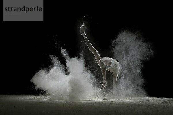 Männlicher Turner macht einen Handstand in einer Wolke aus weißem Staub Ansicht auf schwarzem Hintergrund