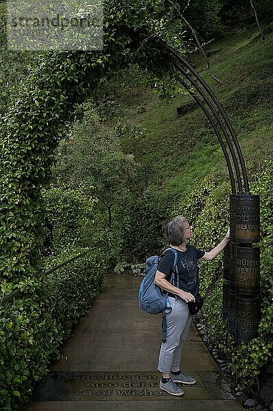 Ältere Frau  Best Ager  dreht an Mühle  Wunschbogen  Bogen  Portal  Tor  Garten für Verliebte  Schloss Trauttmansdorff  Botanischer Garten  Meran  Merano  Südtirol  Autonome Provinz Bozen  Italien  Europa