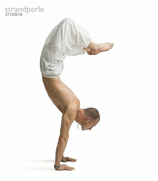 Älterer  hemdloser  muskulöser Mann in weiten Hosen  der einen Yoga Handstand macht  vor weißem Hintergrund