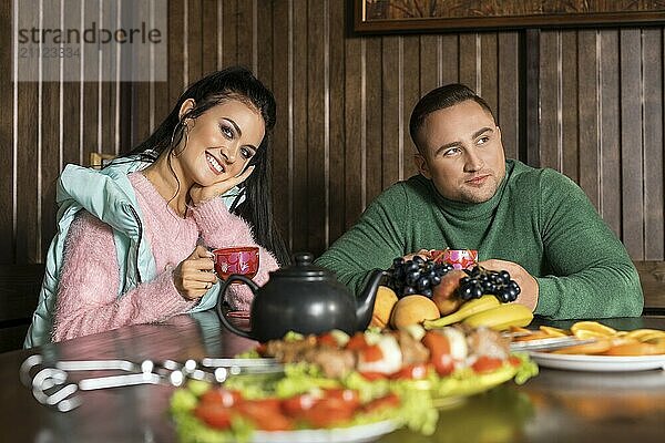 Lächelndes Mädchen in Sportkleidung und ihr gutaussehender Freund in grünem Pullover sitzen am gedeckten Tisch auf der Veranda im Freien