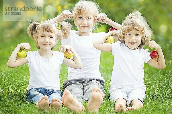 Glückliche Kinder mit Obst sitzen auf grünem Gras im Frühling Park