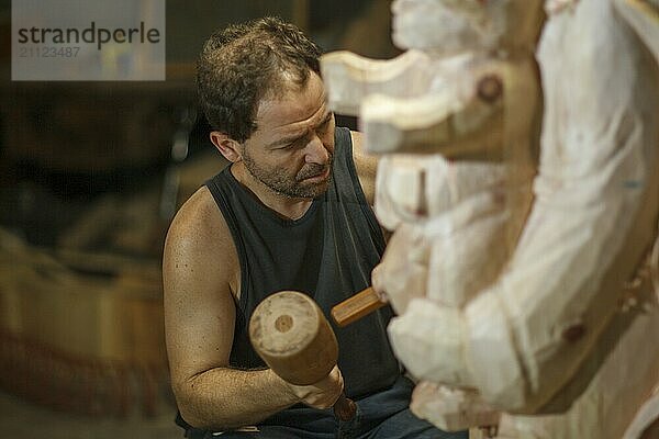 Ein Mann  der sich in einer Werkstatt auf das Schnitzen von Holz mit einem Hammer konzentriert und dabei seine Kunstfertigkeit unter Beweis stellt