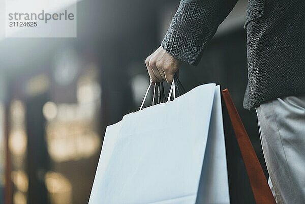 Nahaufnahme eines jungen kaukasischen Mannes  der auf der Straße verschiedene Einkaufstüten aus Papier hält