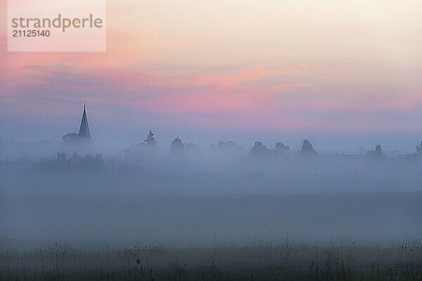 Bezauberndes mystisches Bild mit einem Kirchturm und dem Umriss eines deutschen Dorfes  durch dichten Nebel  bei Sonnenaufgang  in der Nähe von Schwäbisch Hall  Deutschland  Europa