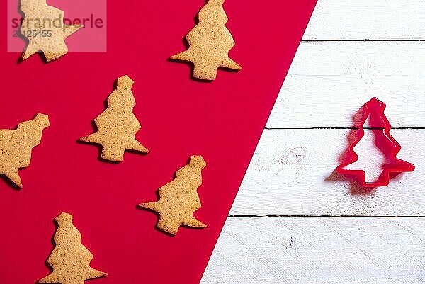 Minimalistisches Konzept für die Weihnachtsbäckerei mit Honig und Ingwerkeksen in Form eines Weihnachtsbaums und einer Ausstechform  auf einem roten und weißen Hintergrund