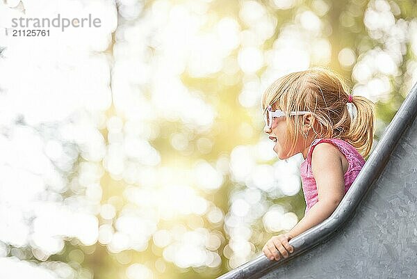 Nahaufnahme eines kleinen Mädchens  das sich auf einer Rutsche auf einem Spielplatz vergnügt  an einem sonnigen Tag