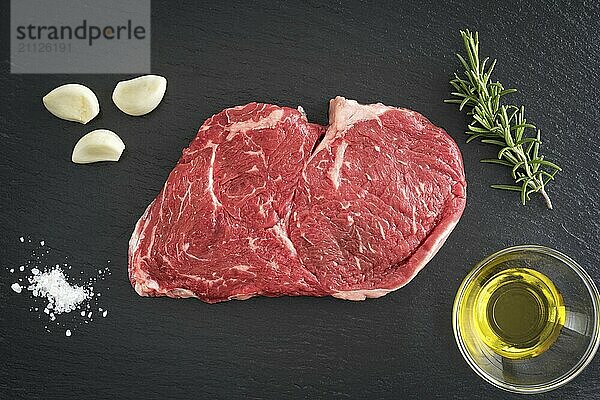 Frisches  ungekochtes Rib Eye Steak mit Knoblauch  Salz  Olivenöl und Rosmarin auf schwarzem Hintergrund