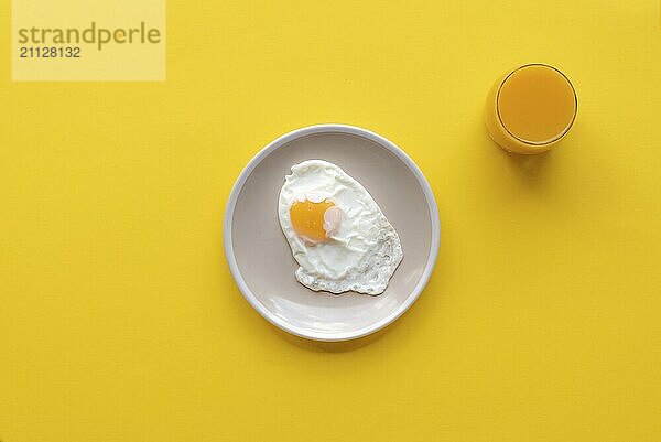 Minimalismus Bild mit einem Spiegelei und ein Glas Orangensaft auf einem gelben Hintergrund