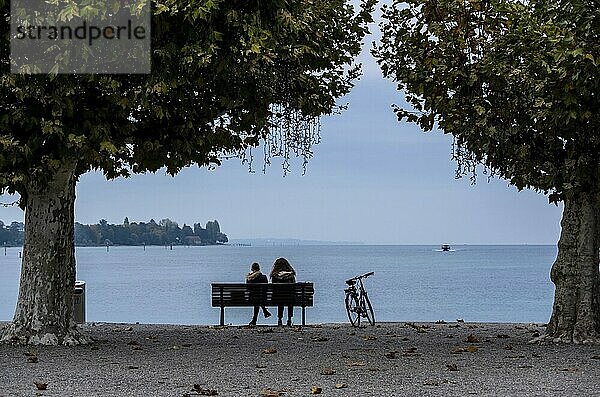 Konstanz am Bodensee. Zwei Personen sitzen auf einer Bank und blicken auf das Wasser