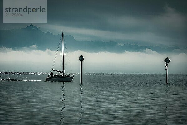 Silhouette eines kleinen Bootes  das auf dem Bodensee in Süddeutschland segelt  und die europäischen Alpen im Hintergrund