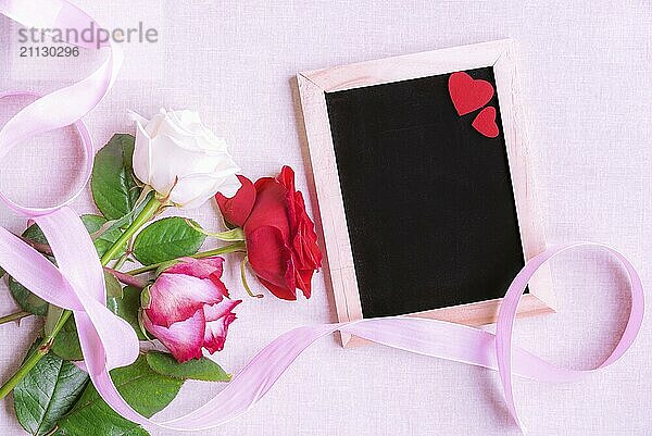 Schöne Bouquet von bunten Rosen  mit einem rosa Band gebunden  in der Nähe eines leeren Kreidetafel mit zwei roten Herzen verziert  auf einem rosa Hintergrund