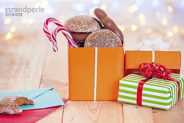 Viele verpackte Geschenke und ein geöffnetes Geschenk mit Lebkuchen und Süßigkeiten  auf einem Holztisch  in der Nähe von Umschlägen  mit Bokeh Lichtern im Hintergrund