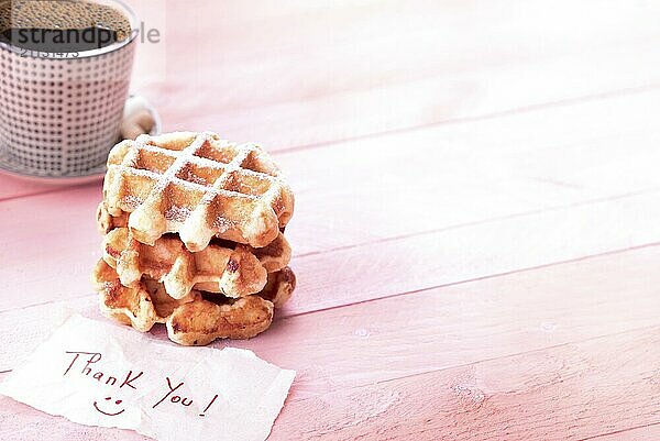 Pikanter Snack mit frisch gebackenen Waffeln mit Puderzucker bestreut  einem Becher Kaffee und einem Gekritzel mit Danke und einem Smiley  auf einem rosa Hintergrund