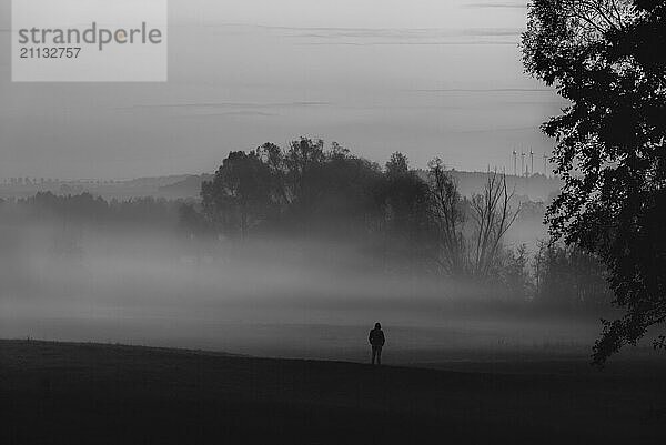 Solitude Thema Bild mit der Silhouette eines Mannes  stehend  allein  in dichtem Nebel  in der Natur  in Deutschland. Schwarz Weiß Bild