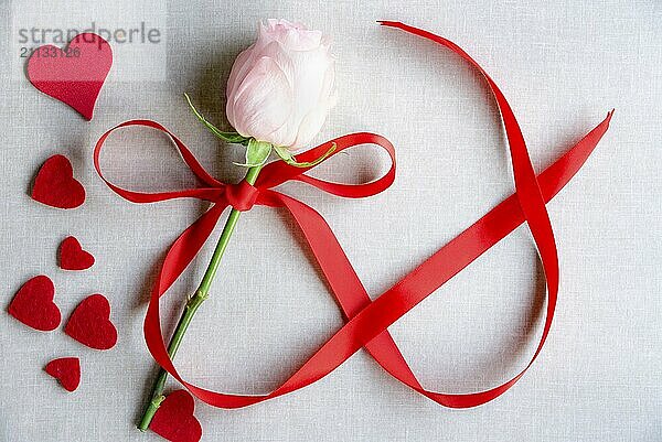 Frauentag Karte Idee mit einer rosa Rose mit Band in Form der Zahl 8 gebunden  umgeben von vielen roten Herzen  auf einem Vintage Stoff Hintergrund