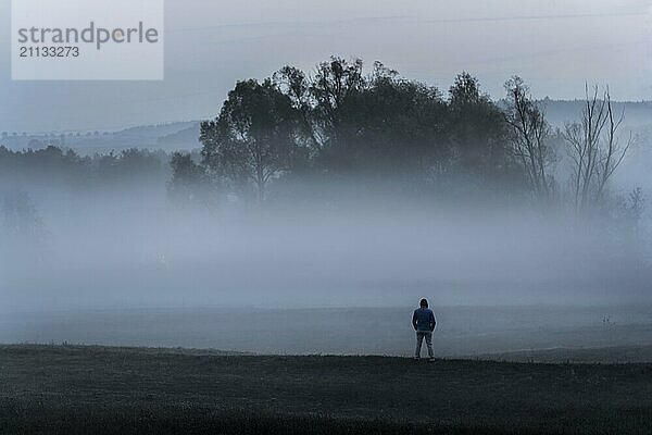 Dramatische Naturlandschaft mit einem Mann  der allein in der Kälte auf einer Wiese steht und in den dichten Nebel blickt  in der Nähe von Schwäbisch Hall  Deutschland  Europa