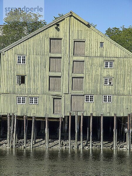 Ein grünes holzgebäude  das auf Pfählen im Wasser steht  mit mehreren Fenstern und Türen  trondheim  norwegen