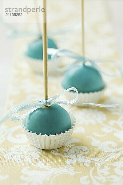 Türkisfarbene Christmas Cake Pops  die kopfüber in Miniatur Muffinförmchen stecken. Sehr geringe Schärfentiefe mit Weihnachtsbeleuchtung im Hintergrund