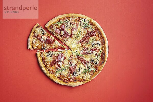 Pizza mit Schinken und Rucola oben Ansicht. Pizza auf rotem Hintergrund flach legen. Leckeres hausgemachtes italienisches Essen. Scheibe Pizza von oben gesehen