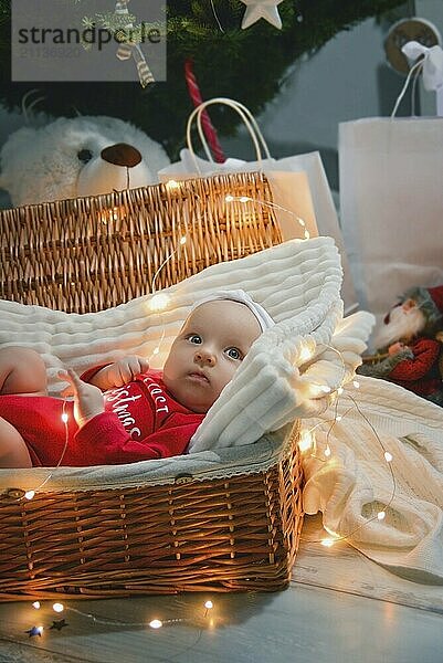 Ein süßes neugeborenes Baby in Weihnachtskleidung schläft in einem Korb auf dem Boden vor einer Weihnachtsdekoration. Silvester