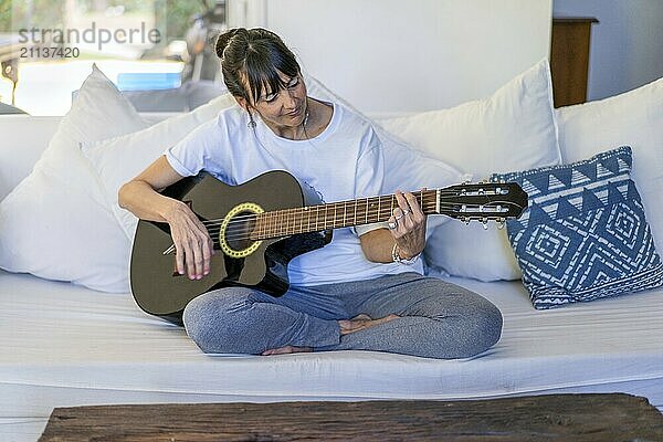 Erwachsene Frau spielt Gitarre  während sie zu Hause auf dem Sofa sitzt