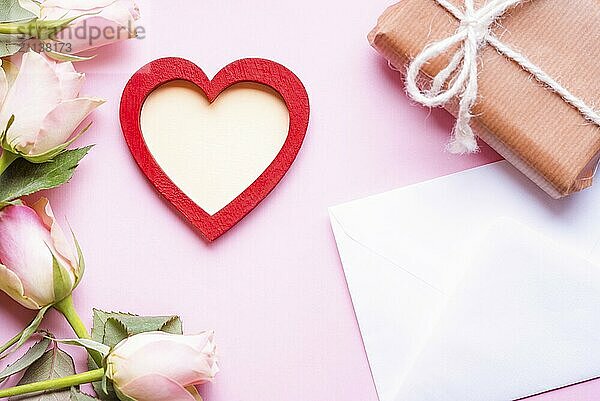 Valentinstag Thema Bild mit einem roten Herzen mit Kopie Raum in der Mitte  umgeben von rosa Rosen  einen Umschlag und ein Geschenk in braunem Papier eingewickelt  auf einem rosa Hintergrund