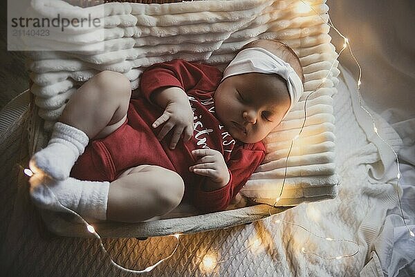 Ein süßes neugeborenes Baby in Weihnachtskleidung schläft in einem Korb auf dem Boden vor einer Weihnachtsdekoration. Silvester