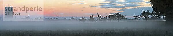 Panorama eines nebligen Herbstmorgens mit den Umrissen eines deutschen Dorfes und einer Baumreihe und einem Waldrand  alles von Nebel bedeckt