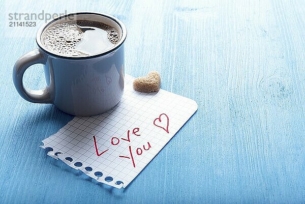 Heißer Kaffee in einer antiken Tasse  Zucker in Herzform und ein Stück Papier mit den Worten Ich liebe dich auf einem blauen Hintergrund im Morgenlicht