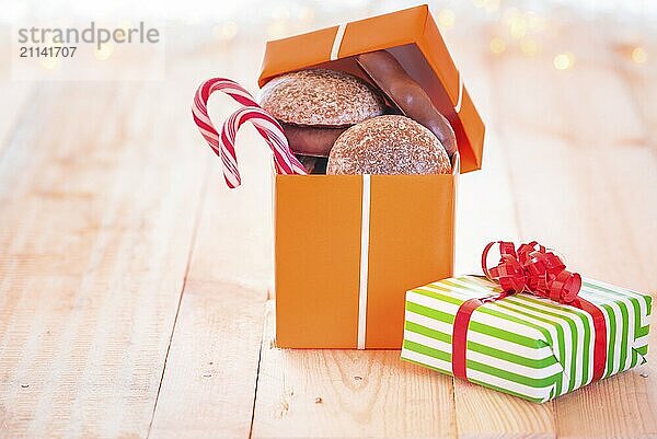 Fröhliches Bild mit einem orangefarbenen Geschenk voll mit Lebkuchen und Süßigkeiten auf einem Holztisch mit leichtem Bokeh im Hintergrund