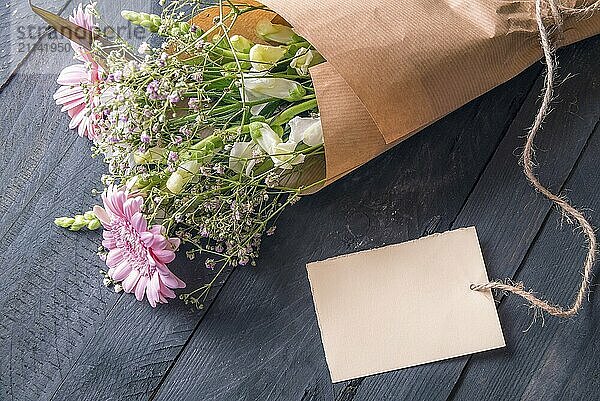 Grußkarten Idee mit einem fröhlichen Blumenstrauß  eingewickelt in altes braunes Papier und einer leeren Etikette  die auf einem rustikalen Holztisch liegt