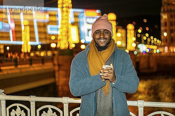 Lächelnder afrikanischer Mann mit einer warmen Tasse Kaffee in der Stadt in der Weihnachtszeit Nacht