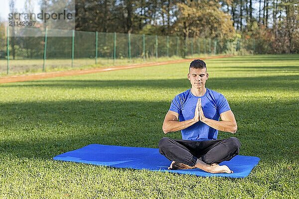 Junger Mann in Sportkleidung sitzt im Park und macht Yoga