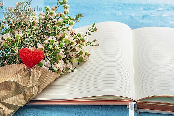 Blumenstrauß aus winzigen weißen Blumen auf einem offenen Tagebuch auf blauem Hintergrund. Frau Bürotisch. Valentinstag Rahmen. Muttertag Feier. Frühling Kontext