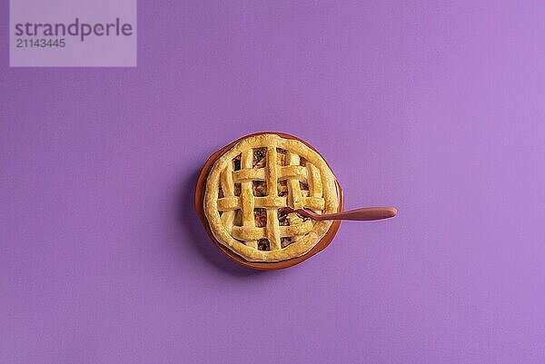 Draufsicht auf einen Apfelkuchen in einem rustikalen Keramiktablett mit einem Teelöffel darin  auf einem lila Hintergrund. Bereit für den Verzehr eines Desserts. Flachlage. Minimalistischer Stil