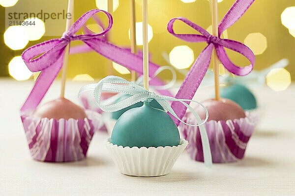 Rosa und türkisfarbene Christmas Cake Pops  die kopfüber in Miniatur Muffinförmchen stecken. Sehr geringe Schärfentiefe mit Weihnachtsbeleuchtung im Hintergrund