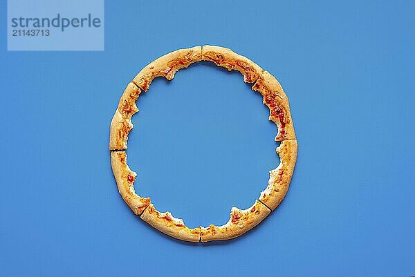 Ansicht von oben mit nur der Kruste von einer Pizza  minimalistisch auf blauem Hintergrund. Pizzareste in einem Kreis auf einem blauen Tisch angeordnet