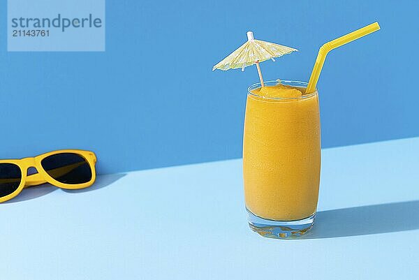 Glas Mango Smoothie und gelbe Sonnenbrille auf einem blauen Hintergrund  in hartem Licht. Sunny Sommertag Kontext. Tropischer Smoothie. Mango Cocktail