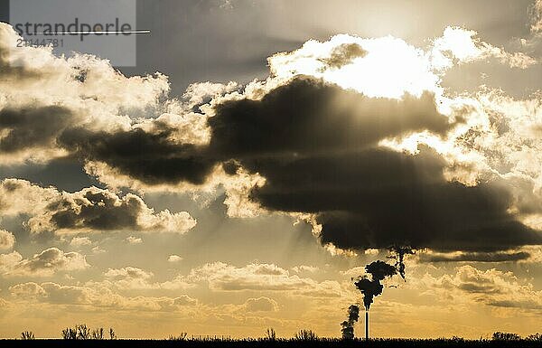 Rauch steigt aus einem Schornstein im Gegenlicht. Wolken im Gegenlicht