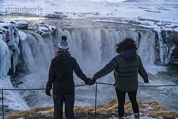 Zwei Menschen stehen auf einem Felsvorsprung und schauen auf einen Wasserfall