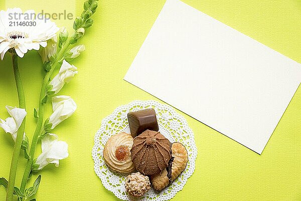 Glückwunschkarte Idee mit einem leeren Papier Note und ein Bündel von leckeren Keksen und Schokolade  weiß schöne Blumen in der Nähe von ihnen  auf einem gelben Hintergrund