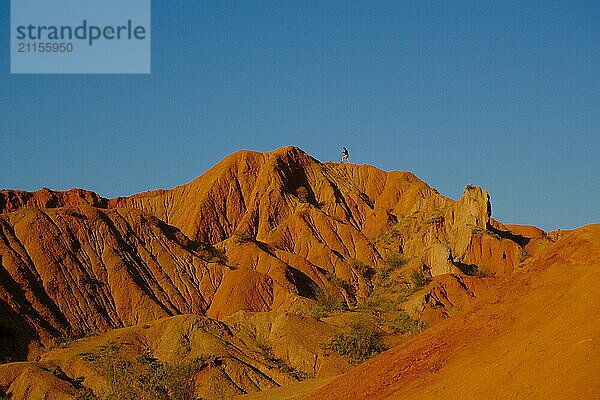 A small figure of a man standing proudly on a high mountain ridge