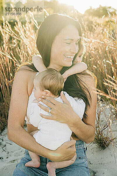 Mother smiling while holding baby  with toddler hugging her