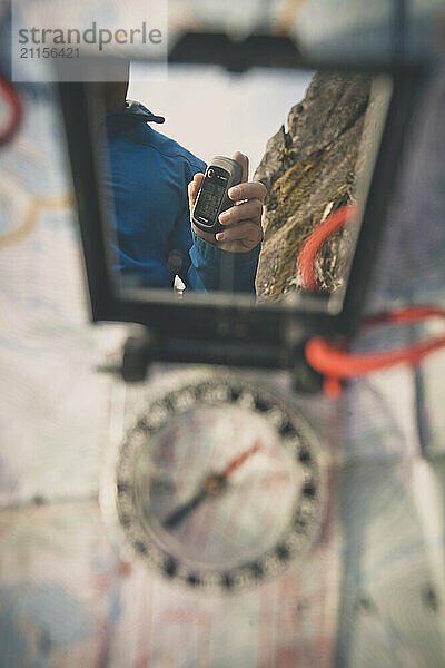 Person holding GPS reflected in mirror of navigation compass